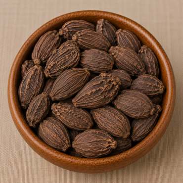 Whole dried black cardamom pods piled in a round wooden bowl on a beige linen surface
