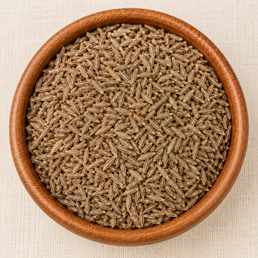 Whole cumin seeds (jeera) filling a round wooden bowl, viewed from above on a linen surface