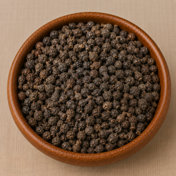 Whole dried cubeb pepper berries with characteristic tails piled in a round wooden bowl