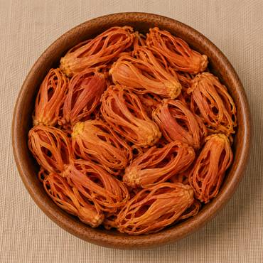 Whole dried mace javitri blades piled in a round wooden bowl on a beige linen surface