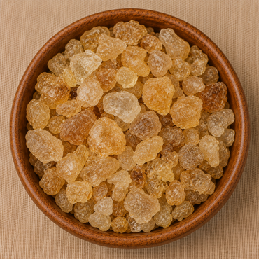 Golden amber gondh edible gum crystals piled in a round wooden bowl on a beige surface
